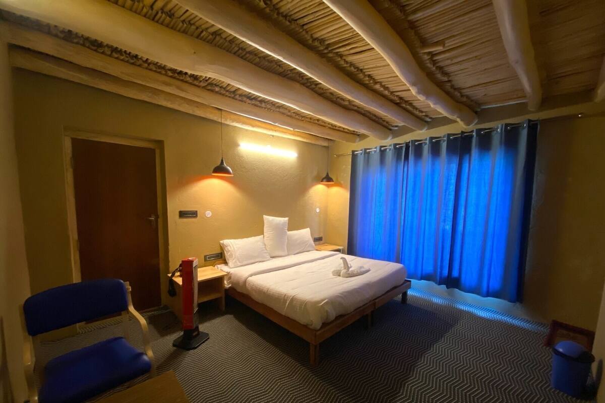 A hotel room with a bed, two bedside lamps, a chair, a desk, and a window with curtains.