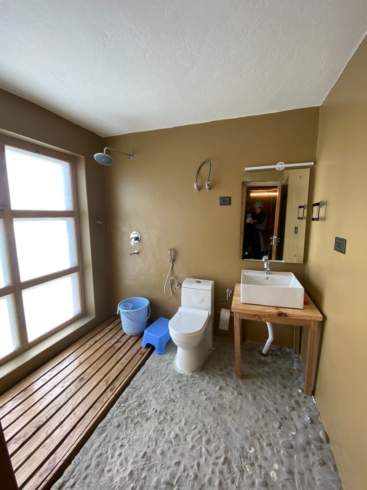 A bathroom with a wooden bench, a toilet, a shower, and a sink.
