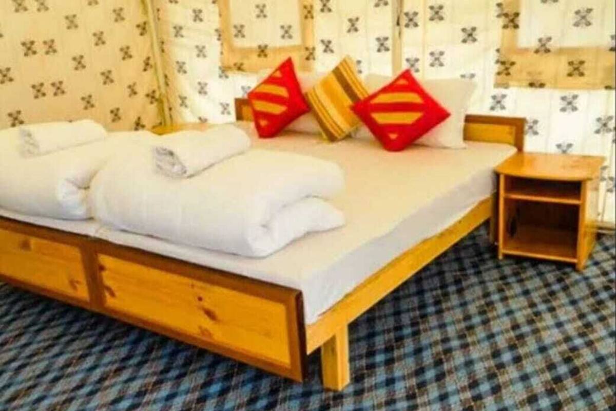 A neatly made bed with white linens and two red pillows, a wooden headboard, and a plaid carpet.