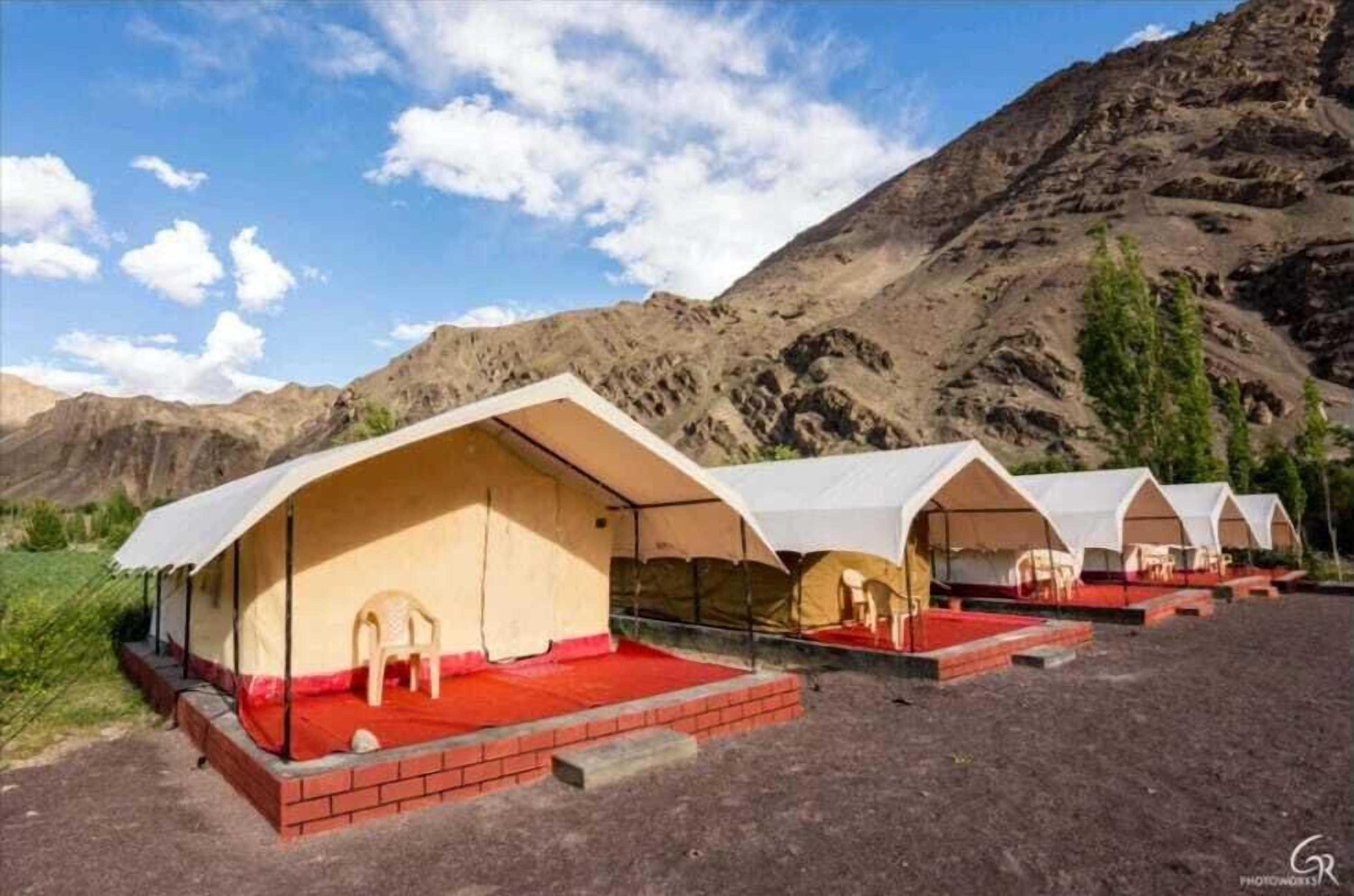 A row of tents with red flooring and white canopies, set against a mountainous backdrop.