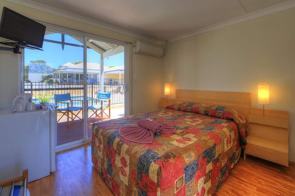 A bedroom with a large bed, a TV, and a view of a pool and outdoor seating area.