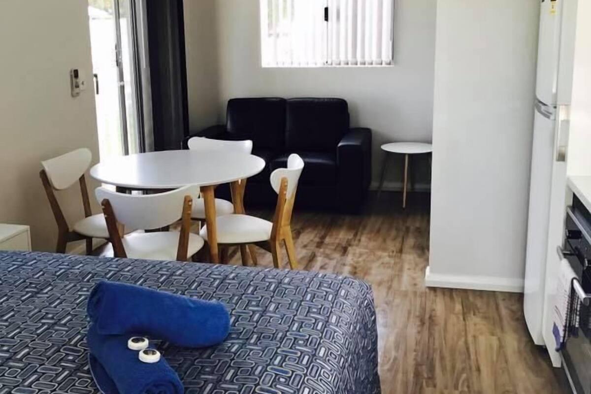 A hotel room with a bed, a dining table with chairs, a sofa, and a refrigerator.