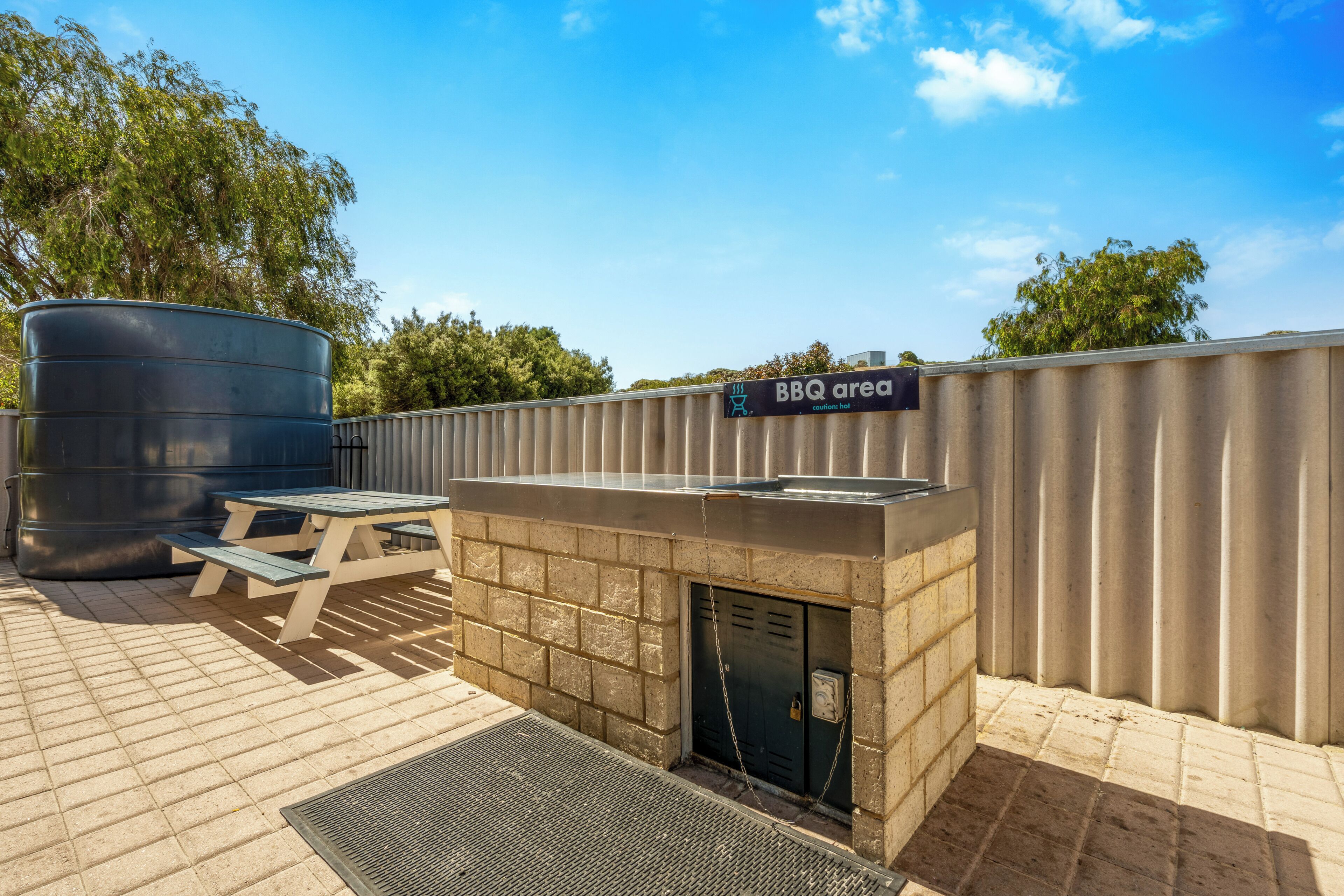 A BBQ area with a grill, a picnic table, and a large water tank.