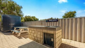 A BBQ area with a grill, a picnic table, and a large water tank.