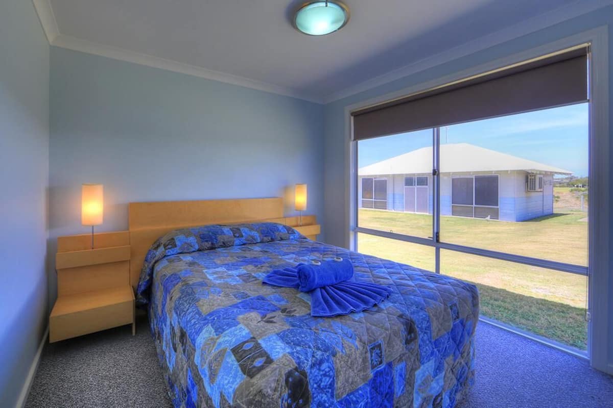 A bedroom with a large bed, a wooden headboard, two bedside lamps, and a view of a building through a large window.