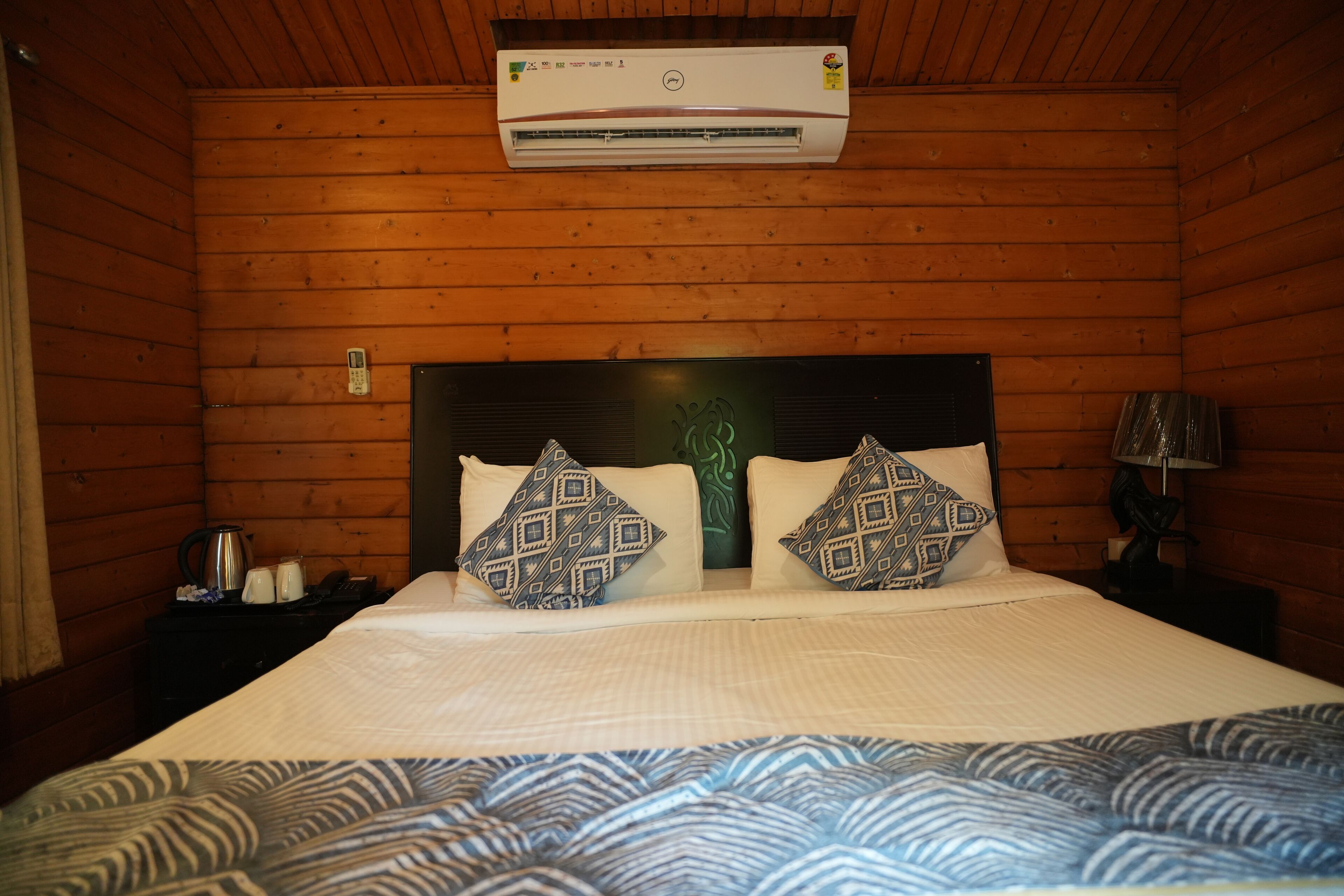 A wooden cabin room with a bed, a nightstand, a lamp, and an air conditioning unit.