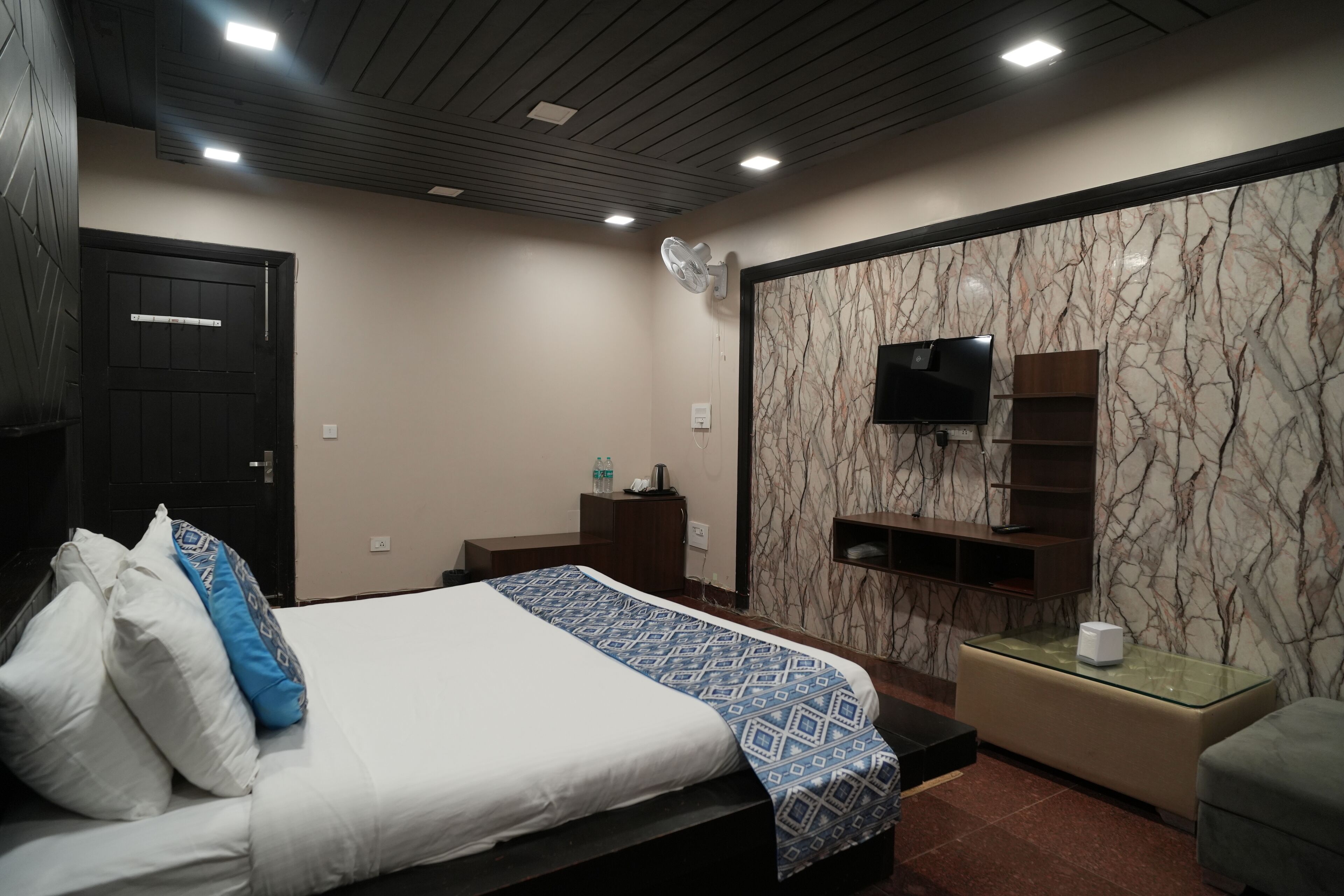 Ein modernes Hotelzimmer mit einem Bett, einem an einer Marmorwand montierten Fernseher, einem kleinen Tisch und einer Sitzecke.