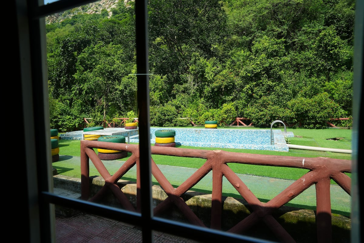 A view of a park with a wooden fence, a fountain, and a pool with blue tiles.