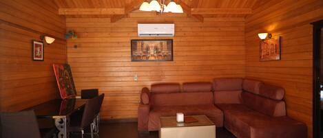 Una stanza con rivestimento in legno, un divano in pelle marrone, un tavolino da caffè in vetro e un tavolo da pranzo con sedie.