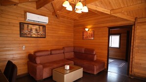Interior de una cabaña de madera con un sofá de cuero, una mesa de centro de vidrio y techo de madera con vigas a la vista.