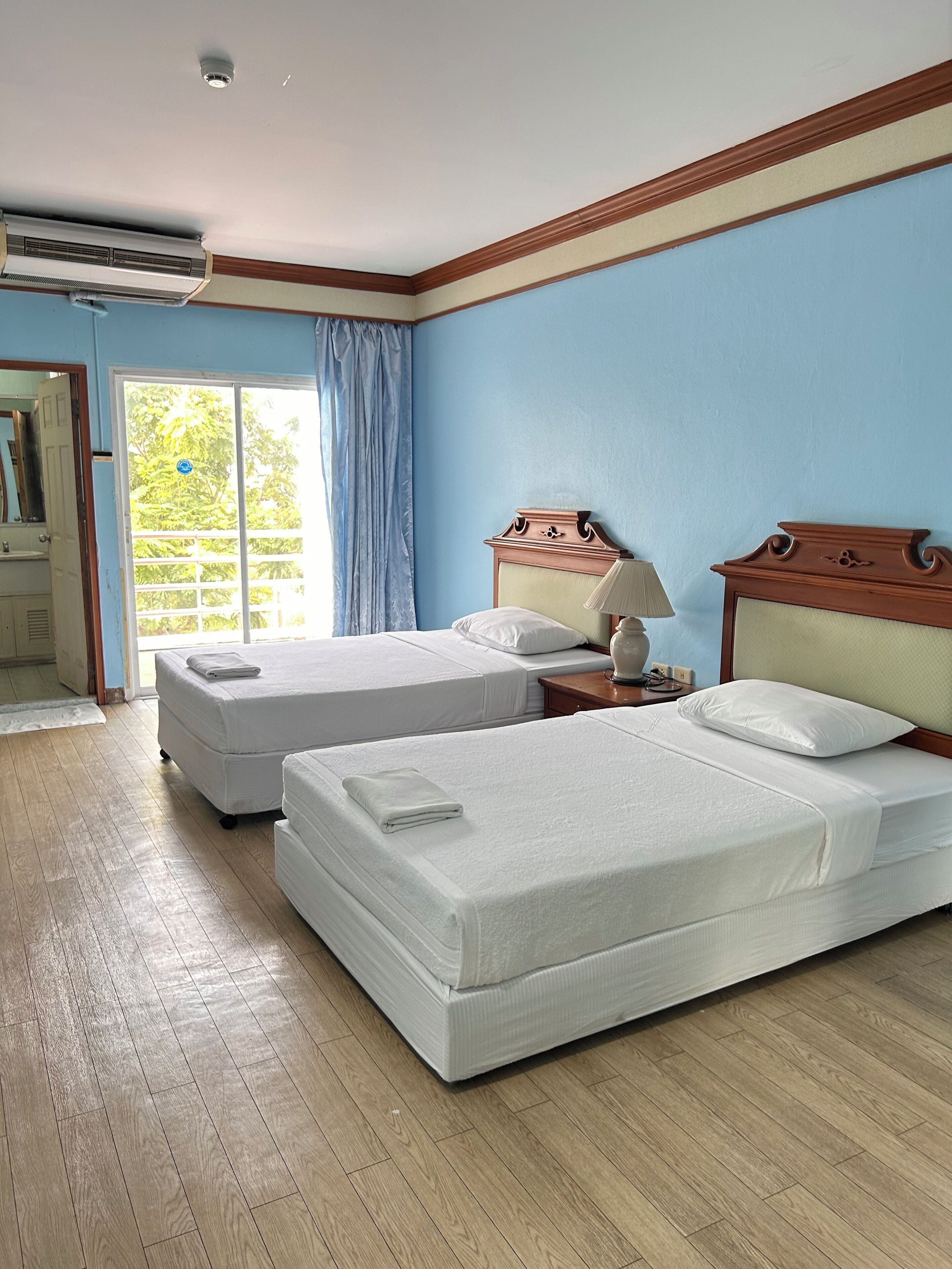 Habitación de hotel con dos camas, una mesita de noche, una lámpara y una ventana con cortinas.