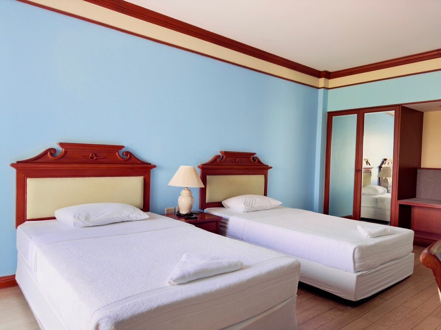 Une chambre d’hôtel avec deux lits, des têtes de lit en bois, une table de chevet avec une lampe et une armoire.