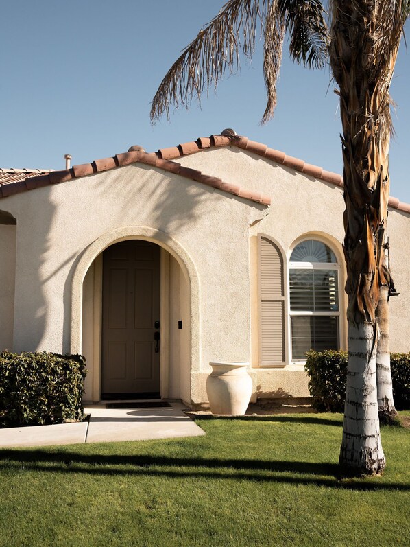 A stucco house with a tiled roof, a large arched entrance, and a palm tree in the foreground.