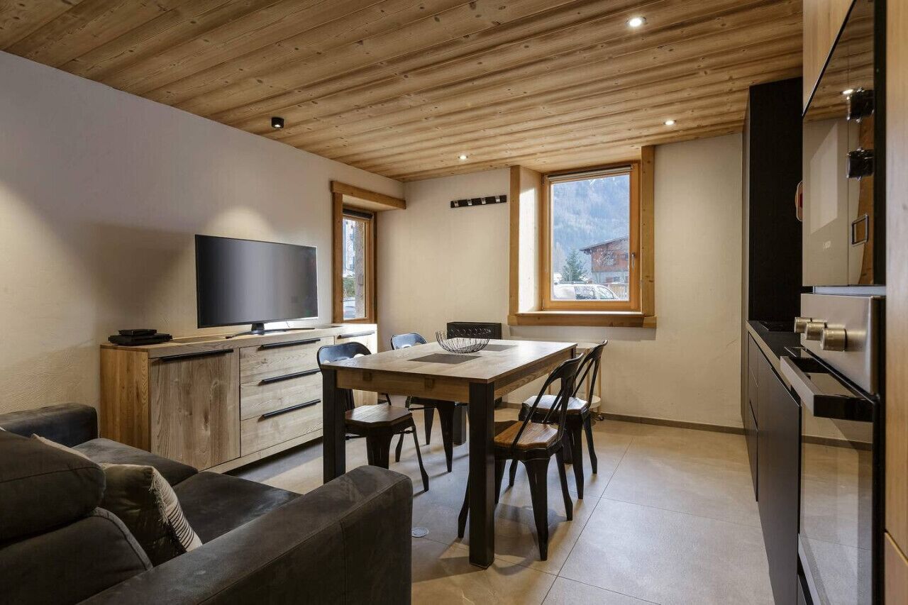 A modern kitchen with a wooden ceiling, a dining area with a table and chairs, a sofa, and a television.