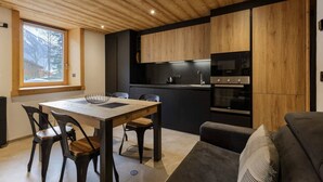A modern kitchen with wooden cabinets, a dining table with chairs, and a built-in oven. - Vouvy - Moderne 4pax | Remontée Flégère 5min | Praz | Arve (Chamonix-Mont-Blanc)