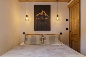 A bedroom with a bed, two hanging light fixtures, a wooden headboard, and a poster of Mont Blanc on the wall. - Vouvy - Moderne 4pax | Remontée Flégère 5min | Praz | Arve (Chamonix-Mont-Blanc)
