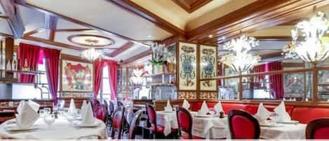 Interior de restaurante con asientos tapizados en rojo, manteles blancos y candelabros.