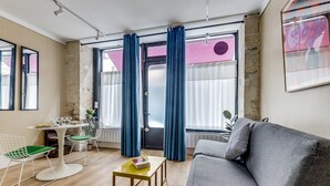 Ett kompakt vardagsrum med en soffa, ett matbord och stolar. Ett fönster med gardiner syns, och en element står på golvet.