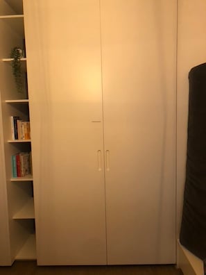 Un placard fermé avec une poignée, une bibliothèque à gauche et un meuble de couleur foncée à droite.