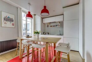 A modern kitchen with white cabinets, a wooden table, and red pendant lights. - The Sweet Night - Modern&Elegant by Mon Petit Faré (Paris)