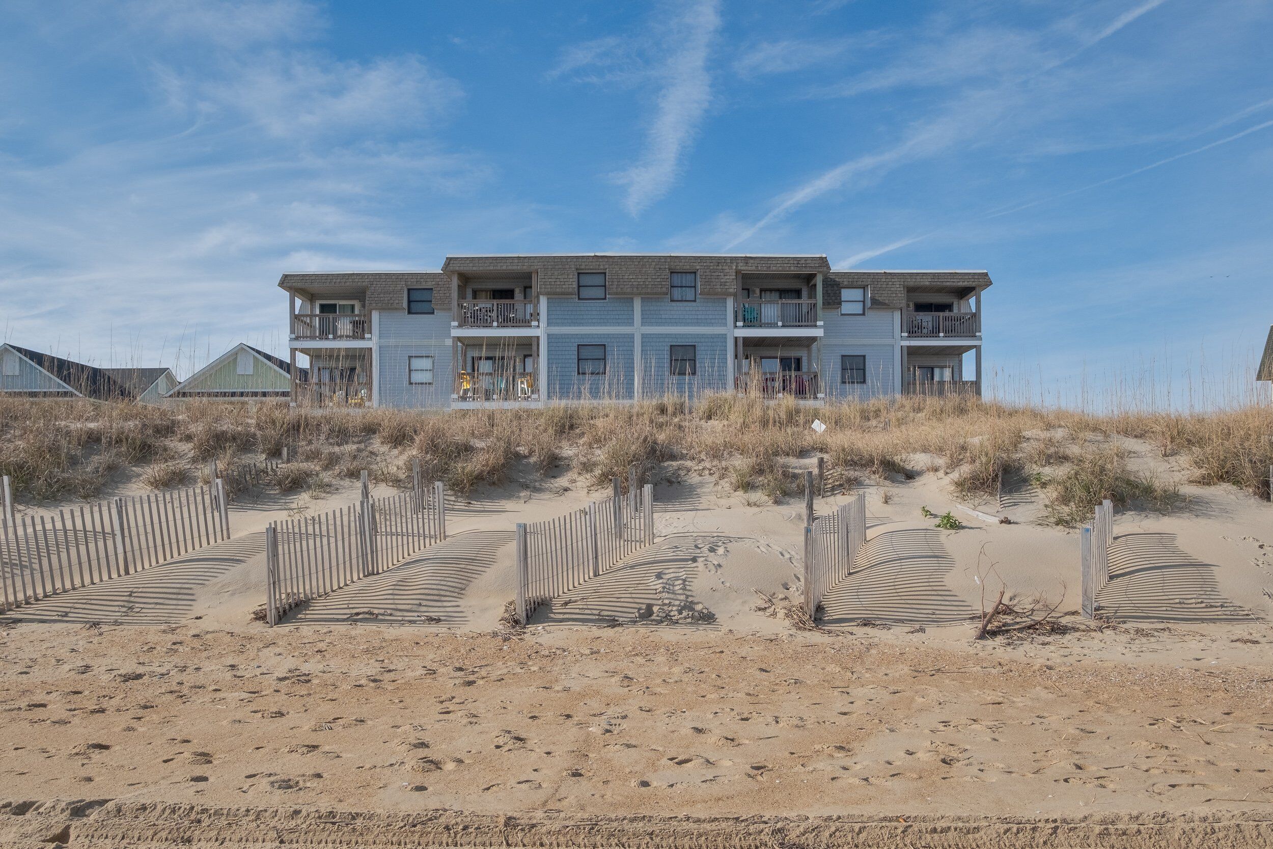 Un edificio a più piani con balconi, affacciato su una spiaggia sabbiosa con passerelle in legno.