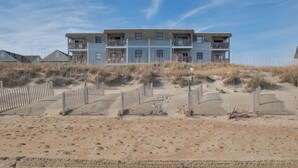 A multi-story building with balconies, situated on a sandy beach with wooden walkways. - 5201 - Flip Flop Time - Cozy Oceanfront Condo | OBX Getaway (Kill Devil Hills)