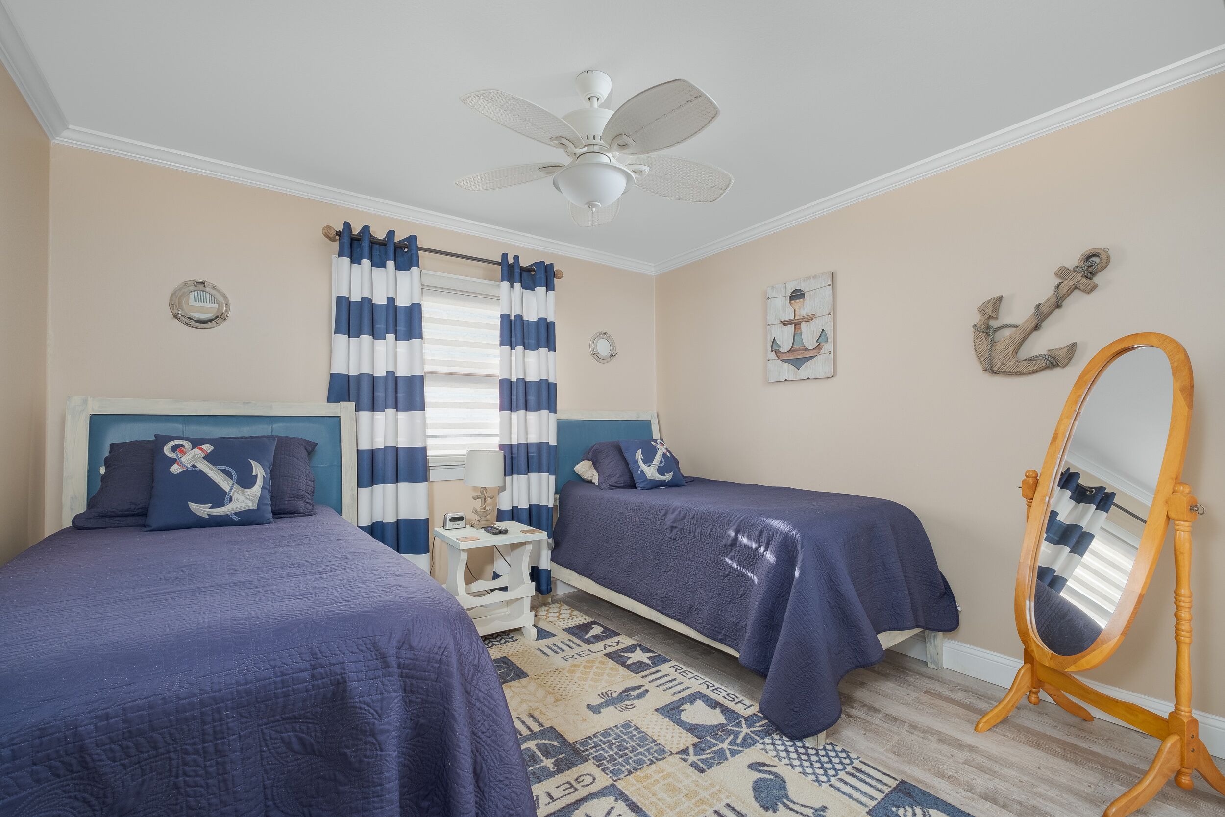 A bedroom with two beds, a ceiling fan, a wooden dresser, and nautical-themed decor.