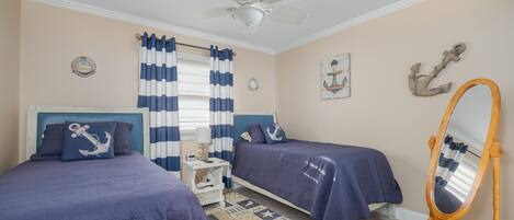 A bedroom with two beds, a ceiling fan, a wooden dresser, and nautical-themed decor.