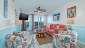 A living room with a red sofa, patterned armchairs, a wooden coffee table, and a ceiling fan. - 5201 - Flip Flop Time - Cozy Oceanfront Condo | OBX Getaway (Kill Devil Hills)