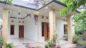 Een huis met een overdekte veranda, meerdere deuren en hangende planten.