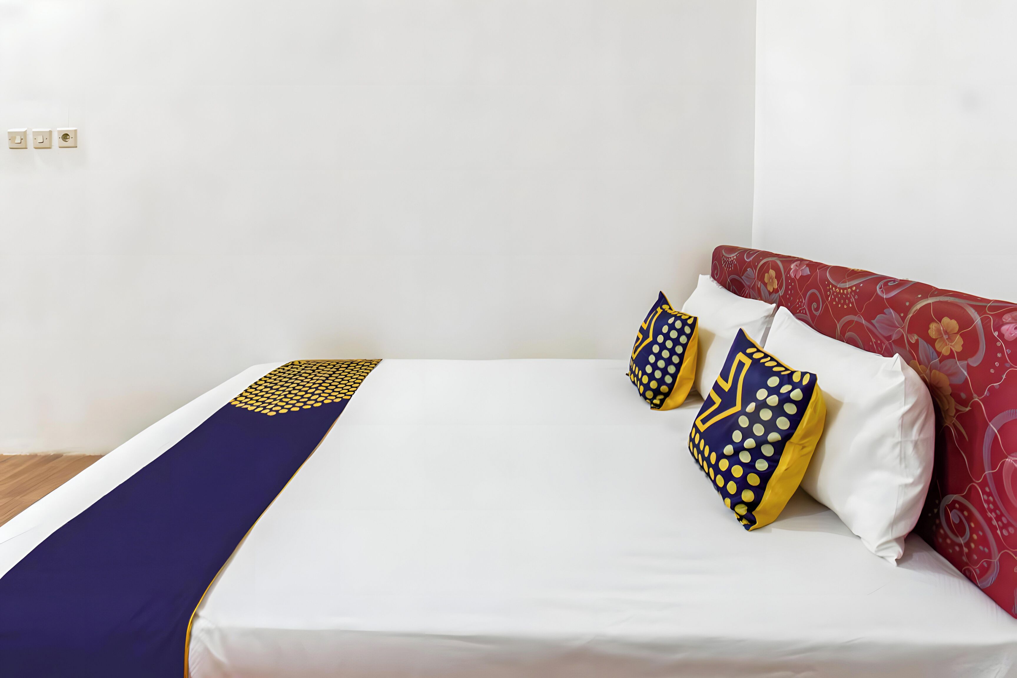 A bed with a white mattress, a blue and yellow patterned bedspread, and two pillows with similar patterns.