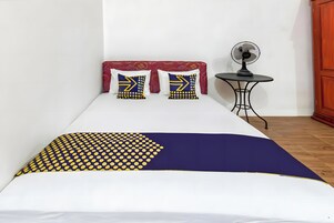 A bed with a patterned bedspread, two pillows with geometric designs, a bedside table with a fan, and a wooden wardrobe.