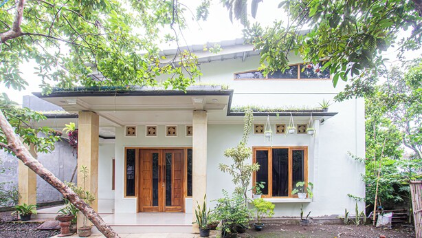 A two-story house with a front porch, wooden doors, and potted plants. - Hotel O Kebun Manis Homestay Near Lapangan Bola Volly Batu Kumbung (Janapria)