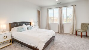 A bedroom with a large bed, a nightstand, a chair, and a window with curtains. - Desert Hot Springs Vacation Home w/ Community Pool (Desert Hot Springs)