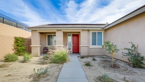 A residential building with a red door, a concrete pathway, and various plants in the yard. - Desert Hot Springs Vacation Home w/ Community Pool (Desert Hot Springs)