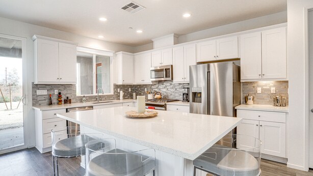 A modern kitchen with white cabinets, stainless steel appliances, and a large island with bar stools. - Desert Hot Springs Vacation Home w/ Community Pool (Desert Hot Springs)