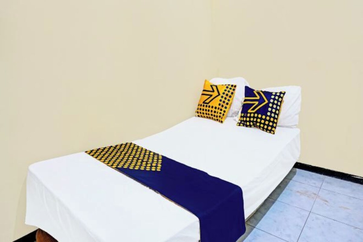 Una cama individual con una colcha blanca, una manta azul y dos almohadas con diseños geométricos.
