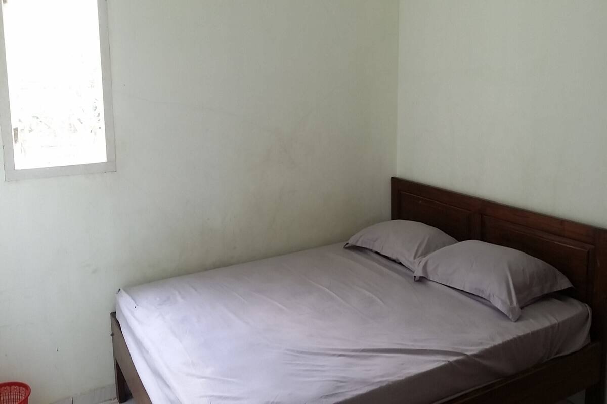 A single bed with a wooden headboard in a room with plain walls and a window.