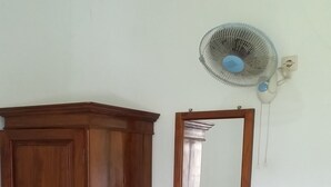 A wooden wardrobe, a mirror, and a bench in a room with a white wall and a ceiling fan.