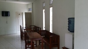 A dining area with a wooden table and benches, a television mounted on the wall, and a water dispenser on a cabinet.