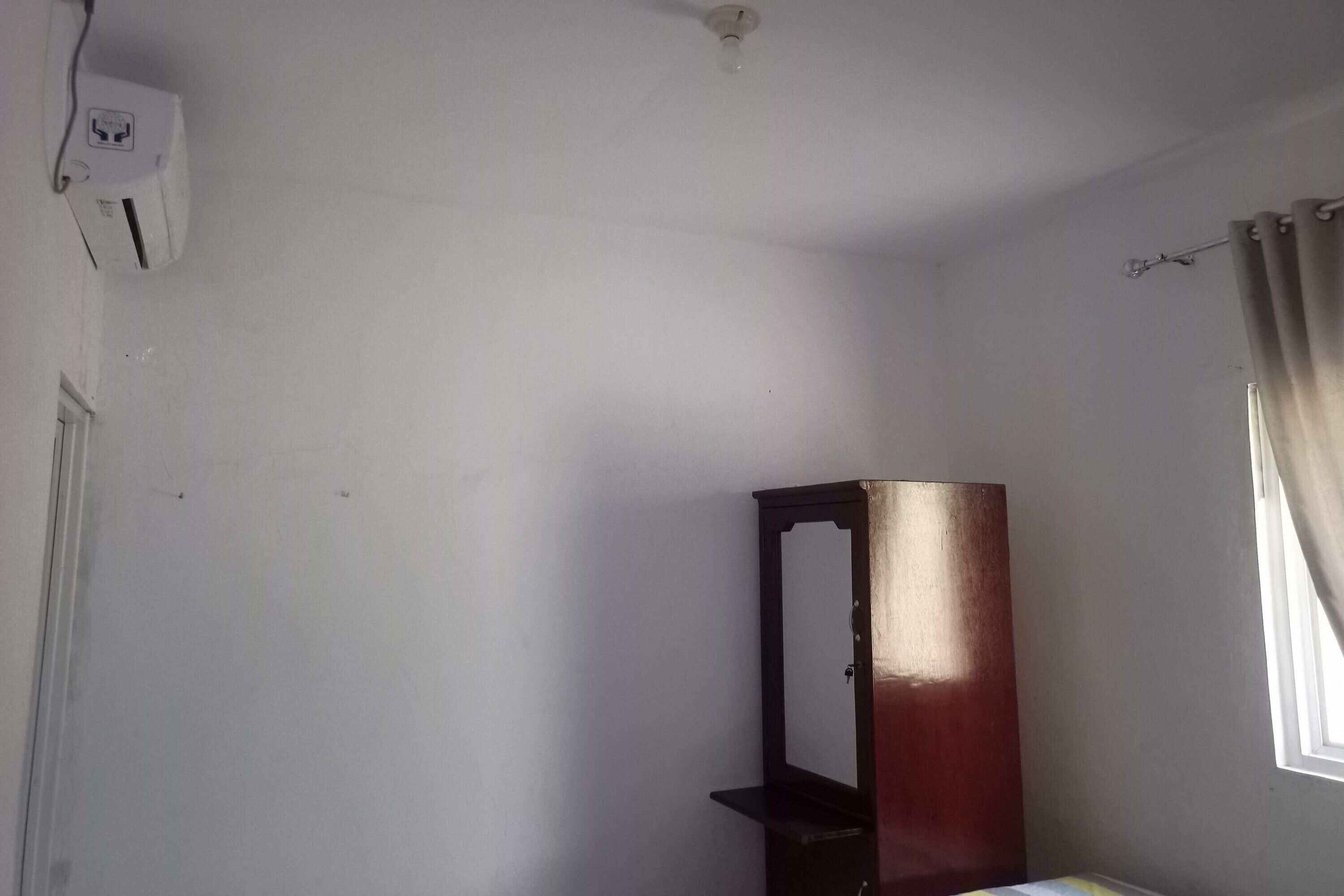 A room with a white wall, a wooden cabinet, a window with curtains, and a ceiling light fixture.