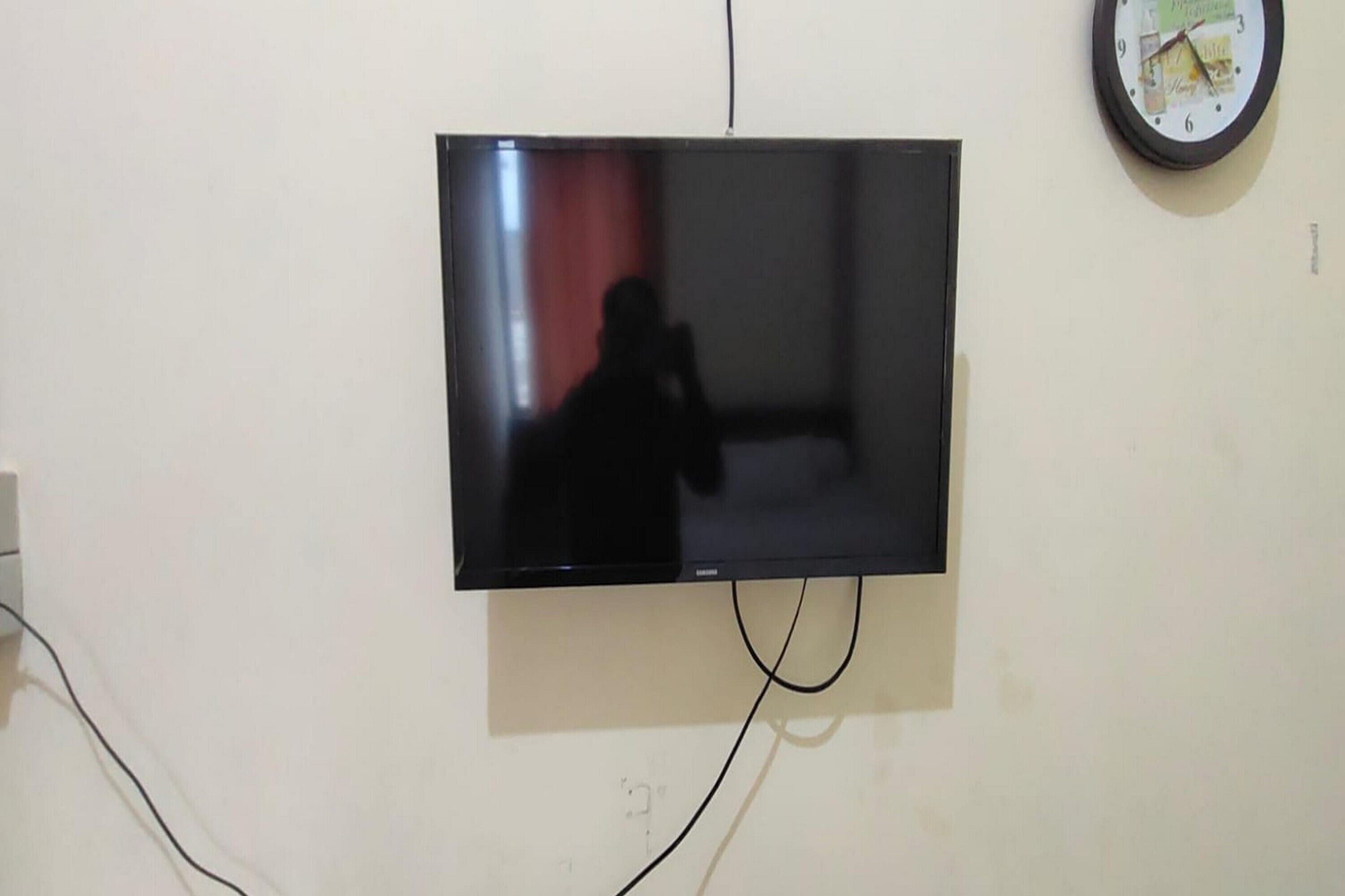 Un téléviseur à écran plat fixé au mur, avec des câbles apparents et une horloge.
