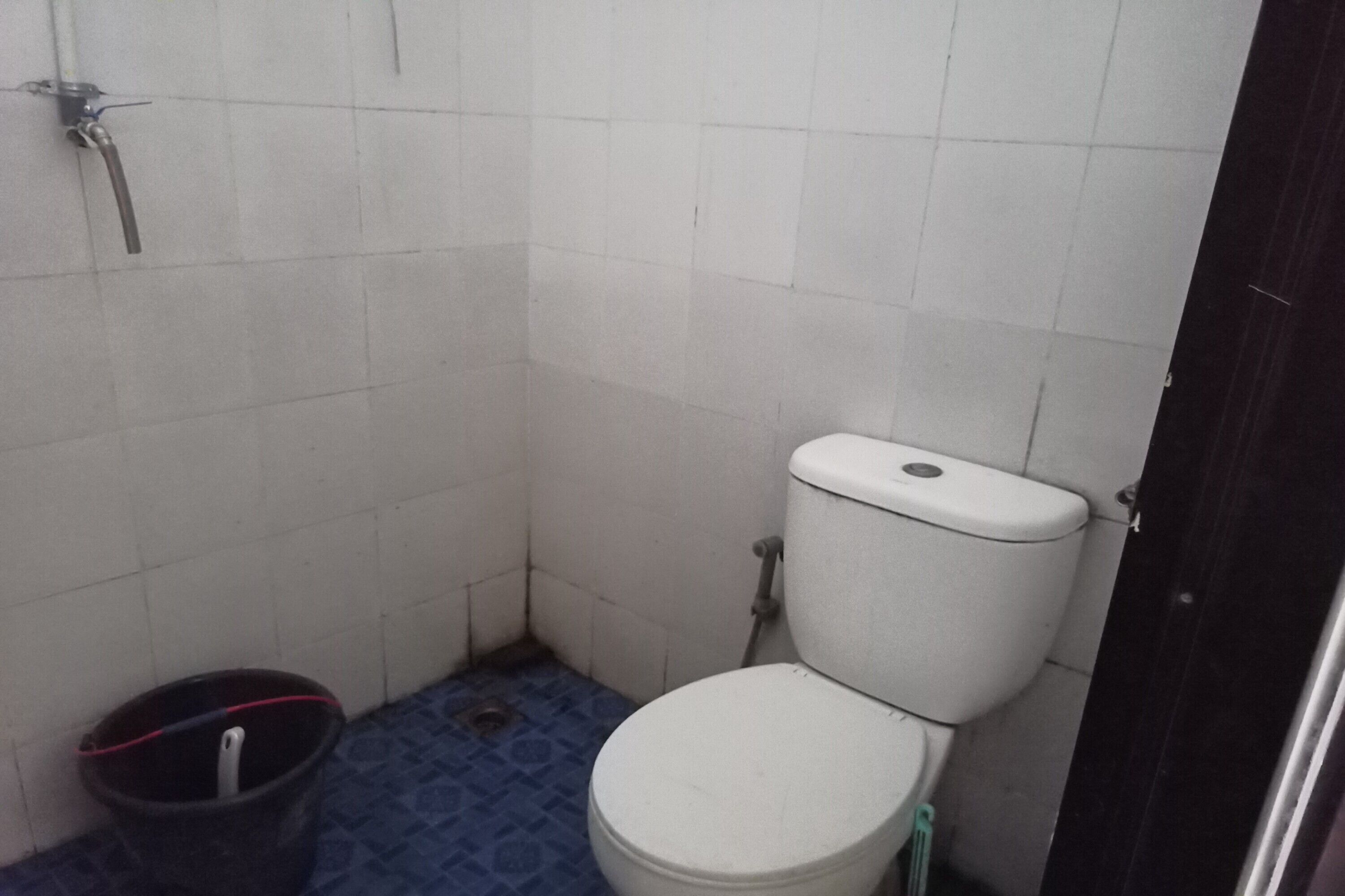 Un baño pequeño y estrecho con un inodoro, una ducha y un balde.