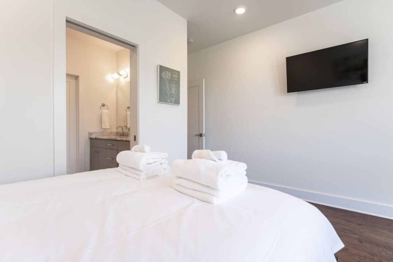 Une chambre d’hôtel moderne dotée d’un grand lit, d’un téléviseur à écran plat fixé au mur et d’une salle de bain visible à travers une porte ouverte.