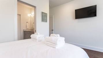 Une chambre d’hôtel moderne dotée d’un grand lit, d’un téléviseur à écran plat fixé au mur et d’une salle de bain visible à travers une porte ouverte.