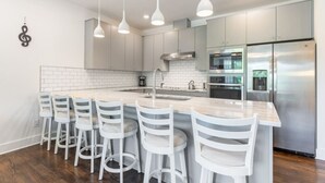 Una cocina moderna con una isla central, electrodomésticos de acero inoxidable y taburetes blancos.