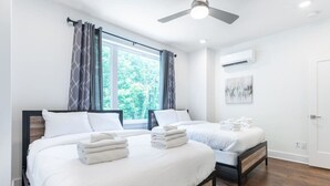 Habitación de hotel con dos camas, ventilador de techo, equipo de aire acondicionado y ventana con cortinas.