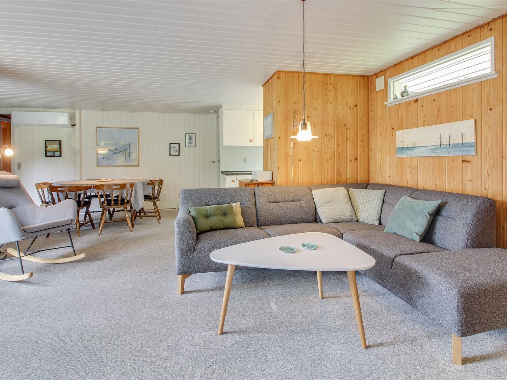 Un salon moderne avec un canapé d’angle gris, une table basse ronde et un coin repas comprenant des chaises et une table en bois.
