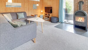 A cozy living room with a grey sofa, a small white table, a TV, and a wood-burning stove. - "Sonia" - 3km from the sea by Interhome (Nørre Nebel)