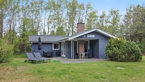 A small, single-story building with a dark blue exterior, a chimney, and a covered patio area with outdoor seating. - "Sonia" - 3km from the sea by Interhome (Nørre Nebel)
